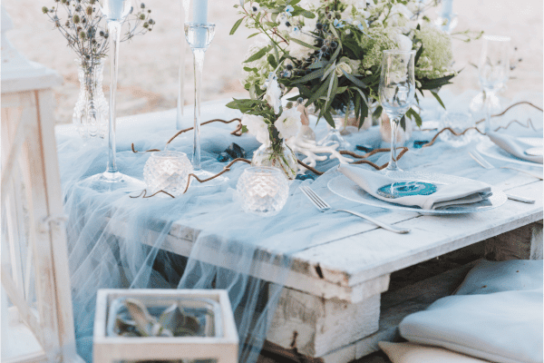  wedding blue cheese cloth mesh draped on a table with glass candlesticks and a greenery heavy centerpiece